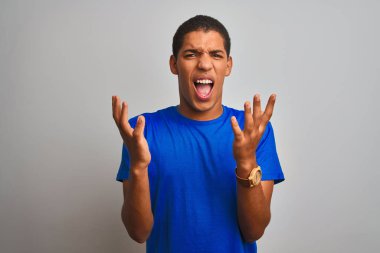 Genç yakışıklı Arap adam izole beyaz arka plan üzerinde duran mavi t-shirt giyen deli ve deli bağırarak ve agresif ifade ve kollar kaldırdı ile bağırıyor. Hayal kırıklığı kavramı.