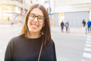 Şehir sokaklarında yürürken heyecanlı gülümseyen güzel genç esmer kadın, şehirde açık havada mutlu ve güven ifade ayakta