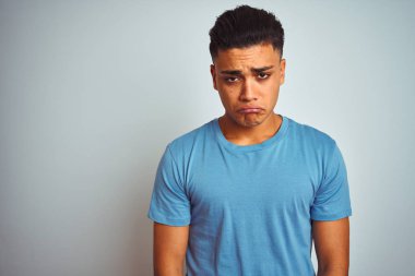 İzole beyaz arka plan üzerinde duran mavi t-shirt giyen genç Brezilyalı adam depresif ve sıkıntı için endişe, kızgın ve korkmuş ağlıyor. Hüzünlü ifade.