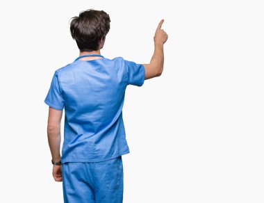 İzole arka plan üzerinde tıbbi üniforma giyen genç doktor parmak eliyle geriye doğru işaret poz