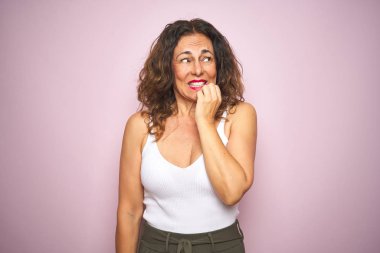 Orta yaş yaşlı kadın pembe izole arka plan üzerinde duran stresli ve ağız tırnak ısırma elleri ile sinir görünümlü. Anksiyete sorunu.