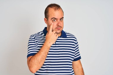 Izole beyaz arka plan üzerinde duran rahat çizgili polo giyen genç adam jest izlerken göz işaret, şüpheli ifade