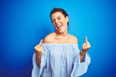 Genç, güzel bir kadın, mavi izole edilmiş arka planda çörek saç stili takıyor orta parmağını gösteriyor ve kötü ifade, provokasyon ve kaba tavır sergiliyor. Heyecanlı çığlık