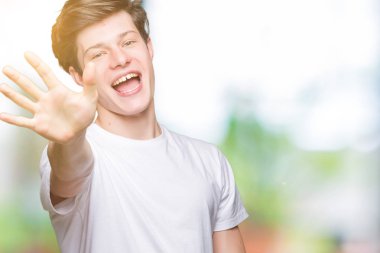 Yakışıklı delikanlı gösterilen ve parmakları ile işaret izole arka plan üzerinde rahat beyaz t-shirt giyen beş kendinden emin ve mutlu gülümseyerek iken numara.