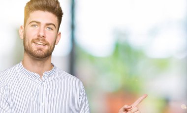 Kameraya bakarak yan el ve parmak ile işaret eden genç yakışıklı adam yüzünde kocaman bir gülümseme ile.