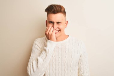 Genç yakışıklı adam izole beyaz arka plan üzerinde duran kış kazak giyen stresli ve ağız tırnakısırma elleri ile sinirli görünümlü. Anksiyete sorunu.