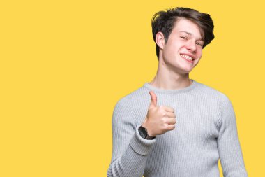 Hareketi el ile mutlu yaşasın yapıyor izole arka plan üzerinde kış kazak giyen genç yakışıklı adam. Başarı gösteren kameraya bakarak ifade onaylama.