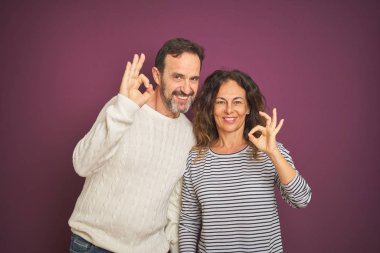 Güzel orta yaş çift izole mor arka plan üzerinde kış kazak giyen olumlu el ve parmaklar ile ok işareti yapıyor gülümseyerek. Başarılı ifade.