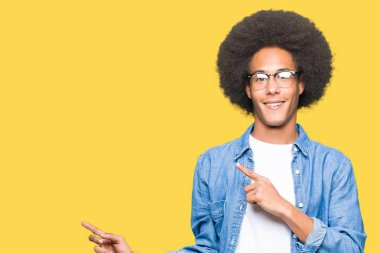 Gülümseyen ve iki elleri ve parmakları ile tarafına işaret kamera bakarak gözlüklü afro saçlı genç Afro-Amerikan adam.