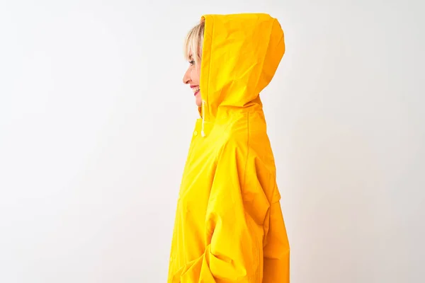Middle age woman wearing rain coat with hood standing over isolated white background looking to side, relax profile pose with natural face with confident smile.