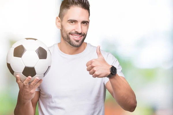 若い男が笑顔の サイン 優秀な兆候を親指をやって幸せな孤立した背景にサッカー サッカー ボールを保持 — ストック写真