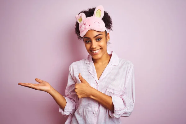 年轻的非洲裔美国妇女穿着睡衣和面具在孤立的粉红色背景显示手掌和做好手势与大拇指 微笑快乐和欢快 — 图库照片