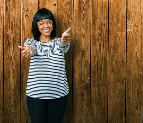 El ile pozitif jest yapıyor onaylama izole arka plan üzerinde çizgili süveter giyen güzel genç Afro-Amerikan kadın başparmak gülümseyen ve başarı için mutlu. Kamera, kazanan jest arıyorsunuz.