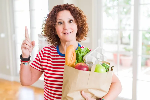 资深女子拿着满满一袋来自超市的新鲜杂货 用一个想法或问题用幸福的脸指指点点 一飞异 — 图库照片