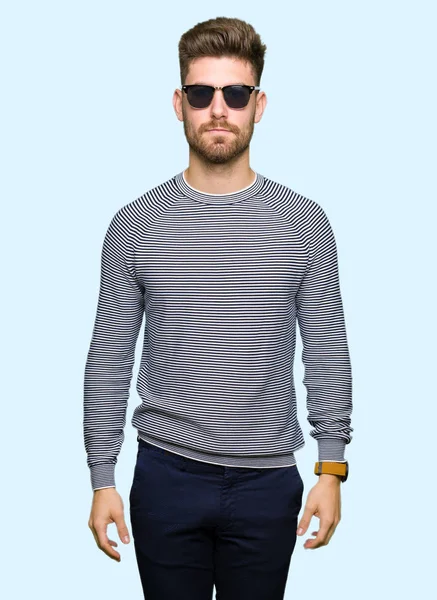 Genç yakışıklı adam yüzünde ciddi bir ifade ile güneş gözlüğü takıyor. Basit ve doğal kameraya bakıyor.