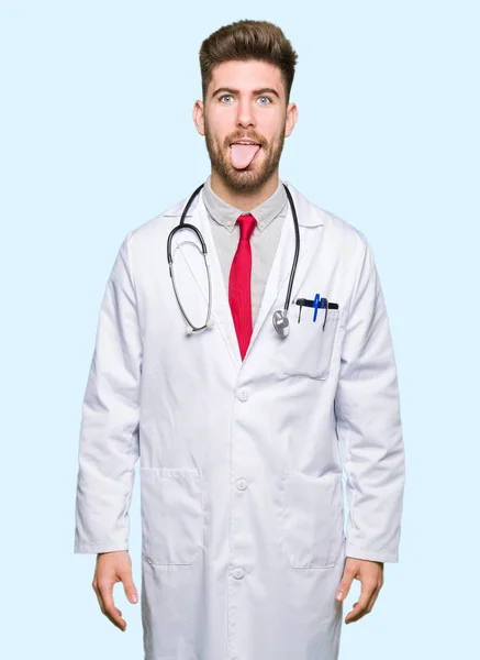 Young Handsome Doctor Man Wearing Medical Coat Sticking Tongue Out — Stock Photo, Image