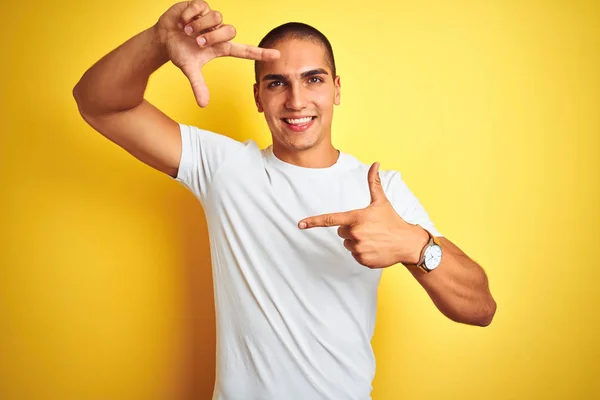 黄色の孤立した背景の上にカジュアルな白いTシャツを着た若い白人男性は 幸せな顔で手と指でフレームを作って笑顔 創造性と写真のコンセプト — ストック写真