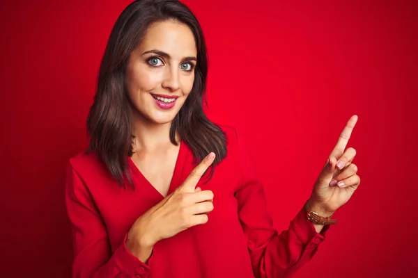 年轻的漂亮女人穿着衬衫站在红色孤立的背景微笑 看着相机指着两只手和手指的一侧 — 图库照片