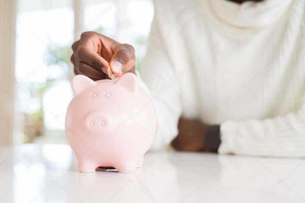 Close up of african man hands putting a coin inside piggy bank, saving money as investment