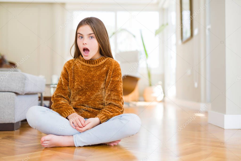 Beautiful young girl kid sitting on the floor at home afraid and shocked with surprise expression, fear and excited face.