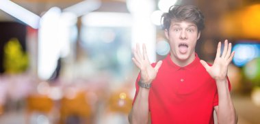 Üzerinde kırmızı t-shirt giyen genç yakışıklı adam deli kutluyor arka plan izole ve silah ile başarı için yükseltilmiş ve açık gözleri heyecanlı çığlık hayrete düşürdü. Kazanan kavramı