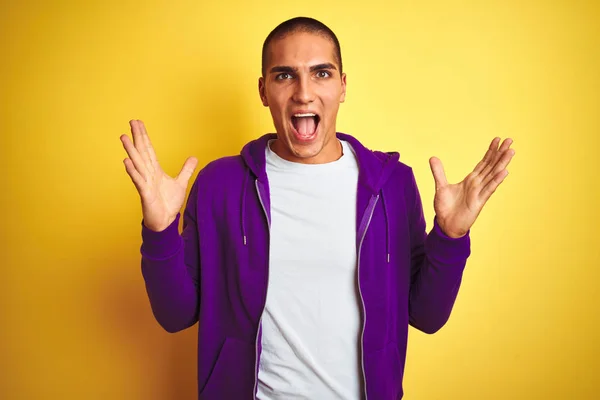 年轻的帅哥穿着紫色运动衫在黄色孤立的背景庆祝疯狂和惊讶的成功与手臂抬起和睁开眼睛尖叫兴奋 优胜者概念 — 图库照片