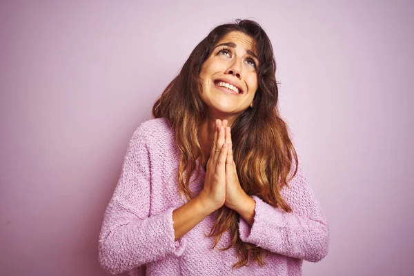 Genç güzel kadın pembe izole arka plan üzerinde duran kazak giyen dilencilik ve umut ifadesi ile birlikte elleri ile dua çok duygusal ve endişeli yüzünde. Af dilemek istiyorum. Din kavramı.