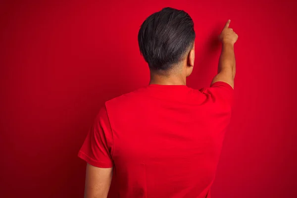 孤立した赤い背景の上に立つTシャツを着た若いブラジル人男性が指の手で前方を向いて後ろ向きにポーズをとる — ストック写真