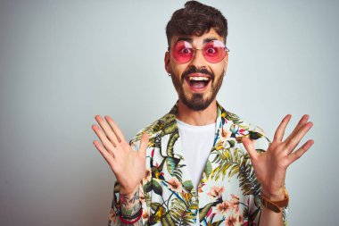Tatilde yazlık gömlek güneş gözlüğü takan adam izole beyaz arka plan üzerinde deli kutluyor ve kollarını kaldırdı ve açık gözleri heyecan çığlık ile başarı için hayran. Kazanan kavramı