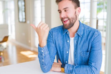 Yakışıklı adam evde mutlu yüz bakarak gülümseyen ve başparmak ile yan işaret.