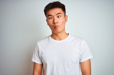 Genç Asyalı Çinli adam izole beyaz arka plan üzerinde duran t-shirt giyen dudakları ile balık yüz yapma, deli ve komik jest. Komik ifade.