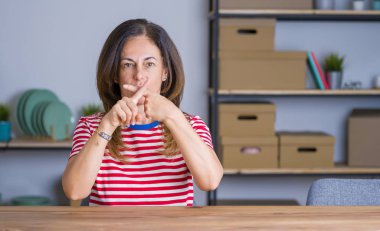 Orta yaş kıdemli kadın evde masada oturan ret ifadesi geçiş parmakları negatif işareti yapıyor