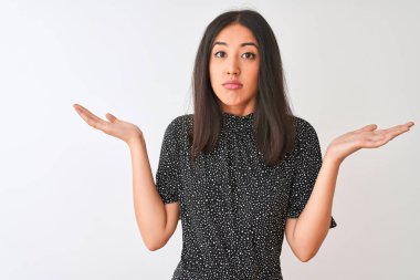 Young chinese woman wearing elegant t-shirt standing over isolated white background clueless and confused expression with arms and hands raised. Doubt concept.