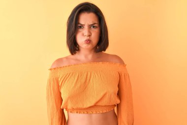 Genç güzel kadın komik yüzü ile yanakları şişirme izole turuncu arka plan üzerinde duran rahat t-shirt giyiyor. Ağız hava ile şişirilmiş, deli ifade.