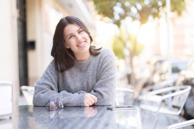 Güzel genç kız neşeli bir kafeteryaya oturan, rahatlatıcı ve şehirde güneş ışığı zevk gülümseyen