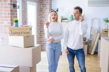 Genç güzel çift başarılı bir fikir ile parmak işaret karton kutular etrafında yeni evde ayakta. Çıktı ve mutlu. Bir numara.