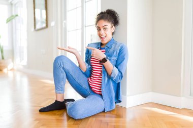 Hayret ve el ile sunulması ve parmak ile işaret ederken kameraya gülümseyen katta oturan afro saçlı güzel genç Afro-Amerikan kadın.