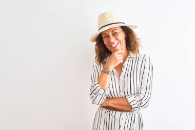 Izole beyaz arka plan üzerinde çizgili elbise ve şapka giyen orta yaş iş kadını çapraz kollar ve el çene kaldırdı gülümseyerek kamera emin görünümlü. Olumlu düşünme.