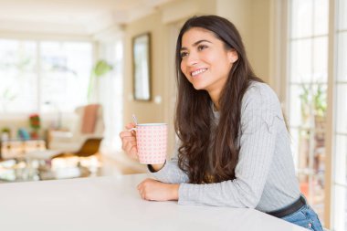 Güzel genç kız evde bir fincan kahve içme ve gülümseyerek
