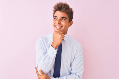 Genç yakışıklı işadamı gömlek giyen ve kravat üzerinde duran izole pembe arka plan üzerinde el çene si soru, dalgın ifade düşünme. Gülümseyen ve düşünceli bir yüz. Şüphe kavramı.