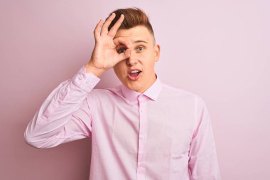 İzole pembe arka plan üzerinde duran zarif gömlek giyen genç yakışıklı işadamı ok jest yaparak şaşırmış yüzü ile şok, parmaklardan bakarak göz. İnanmayan ifade.