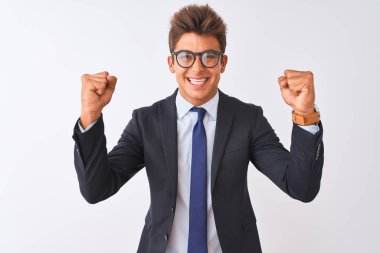İzole beyaz arka plan üzerinde takım elbise ve gözlük takan genç yakışıklı işadamı, kollarını kaldırıp gözleri açık bir şekilde başarıya uğrup için sürpriz ve şaşkınlık yarattı. Kazanan kavramı.
