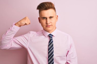Genç yakışıklı işadamı gömlek ve kravat izole pembe arka plan güçlü kişi kol kas gösteren, emin ve güç gurur üzerinde duran giyiyor