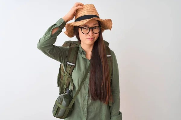 Chinese hiker woman wearing canteen hat glasses backpack over isolated white background confuse and wonder about question. Uncertain with doubt, thinking with hand on head. Pensive concept.