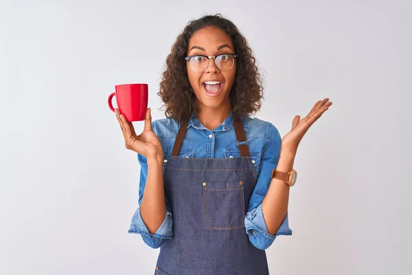 Brazilian barista woman wearing apron drinking cup of coffee over isolated white background very happy and excited, winner expression celebrating victory screaming with big smile and raised hands