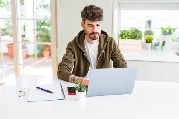 Young student man using computer laptop and notebook with a confident expression on smart face thinking serious
