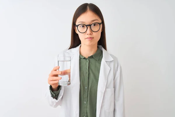 真剣に考えるスマートな顔に自信を持った表情で孤立した白い背景の上に水を飲むメガネをかけた若い中国のドゥークター女性 — ストック写真