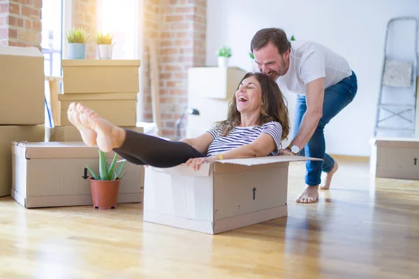 Middle age senior romantic couple having fun riding inside of cardboard, excited and smiling happy for moving to a new home