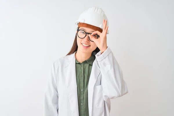 孤立した白い背景の上にコートヘルメットのメガネをかけた若い中国人エンジニアの女性は 手を笑顔でOkジェスチャーを行い 幸せそうな顔で指を通して目を見る — ストック写真