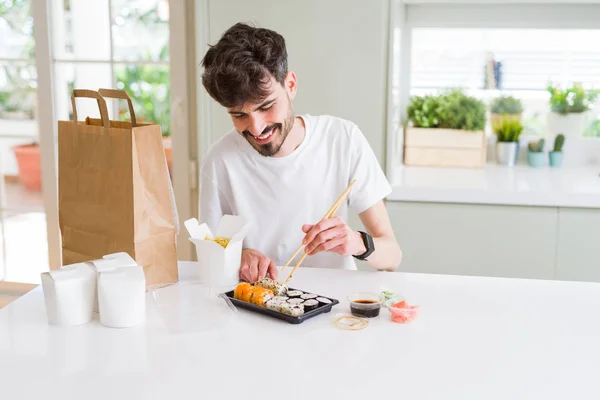 Young man eating sushi asian food and noodles using choopsticks from take away delivery